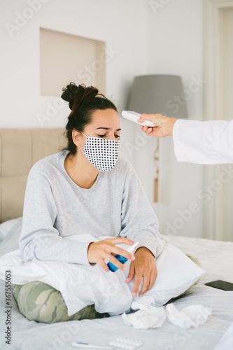 Vertical shot of a female wearing a mask having her fever checked by a nurse
