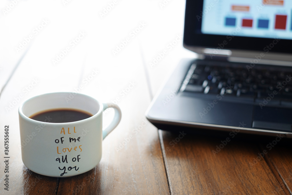 coffee cup with love message on a wooden table and a computer out of focus in the background coffee cup with love message on a wooden table and a computer out of focus in the background