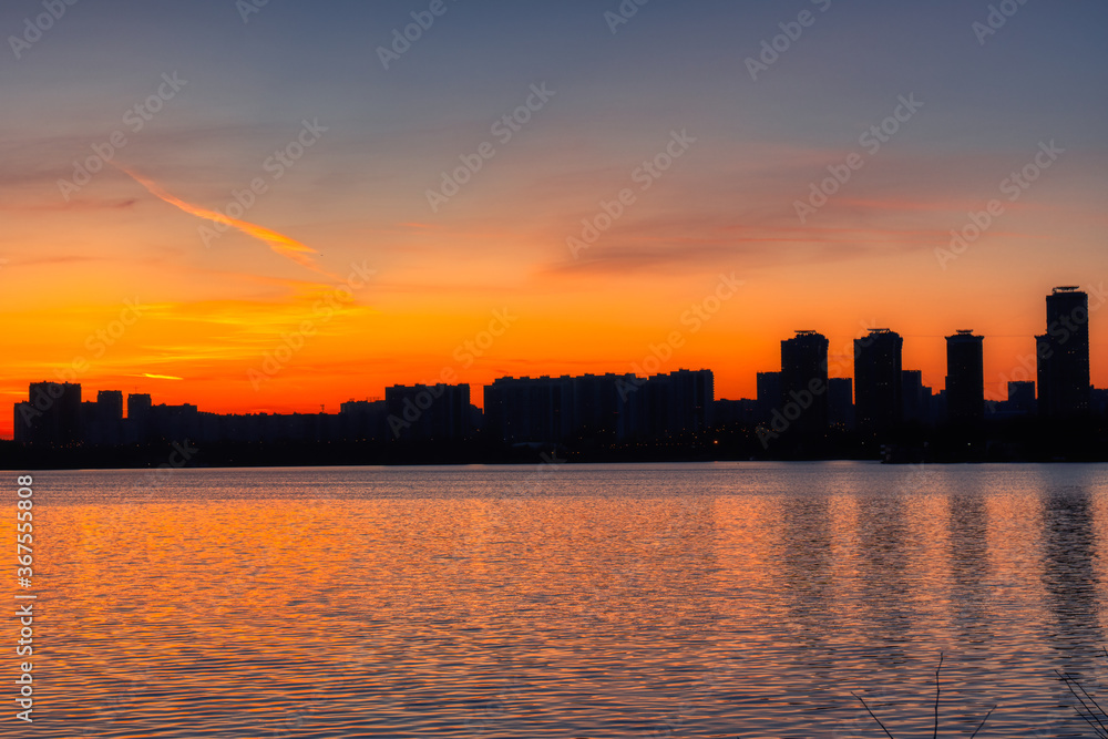 Silhouette of urban buildings on the background of an orange sunset reflected in the water of the bay