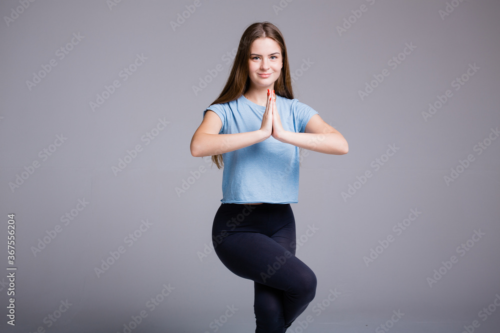 A young woman in yoga clothes stands on one leg and meditates with her palms together in front of her. Sporty woman with long hair. A young woman in yoga clothes stands on one leg and meditates with her palms together in front of her. Sporty woman with long hair.
