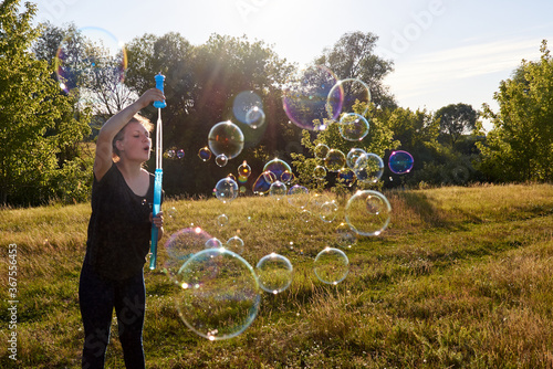 Woman blowing soap bubbles on the meadow in summer.