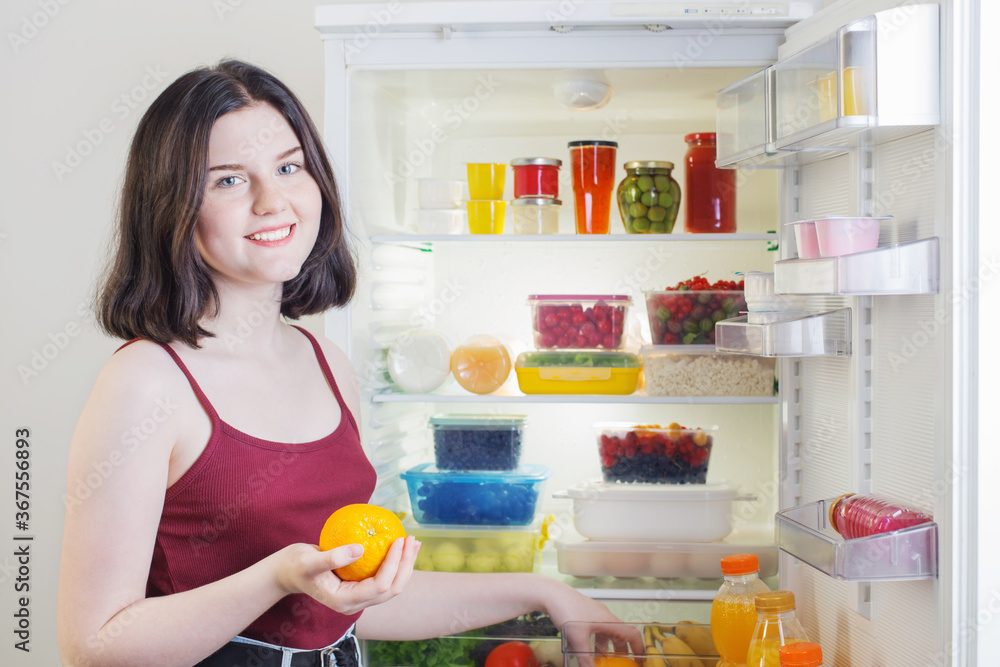 smile girl with orange near open refrigerator