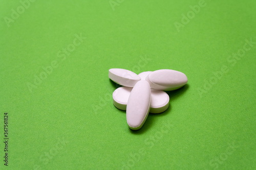 Heap white pills, drugs on a green background close up, macroshot tablets, isolated. Pandemic medications. Drugs disease treatment - covid-19, coronavirus. Vitamins for human health photo