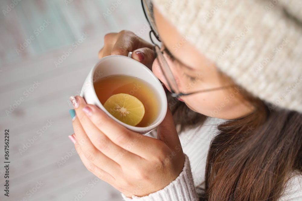 Woman's hand holding a Warm cup of hot honey lemon tea with a beautiful manicure and knitting sweater. Concept of Drink, fashion, morning.