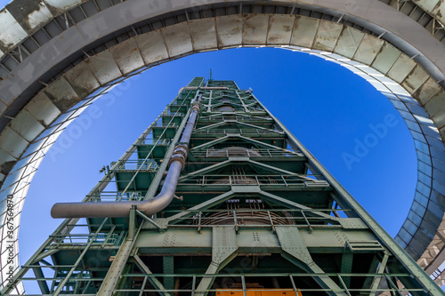 A bottom-up wide-angle view of an abandoned old refinery tower made of steel with its round ramp framing the image in a sunny day with a blue sky in Lisbon, Portugal.