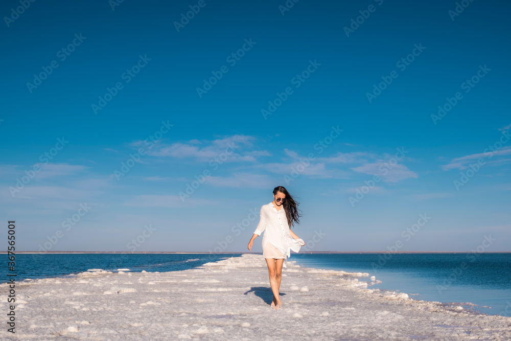A beautiful woman walks along the seashore in a beach dress. A beautiful woman walks along the seashore in a beach dress.
