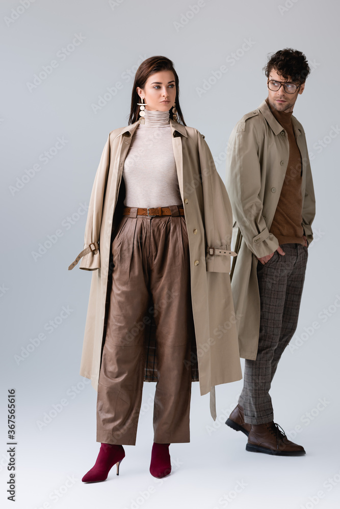 full length view of handsome, stylish man looking at fashionable woman while holding hand in pocket on grey full length view of handsome, stylish man looking at fashionable woman while holding hand in pocket on grey