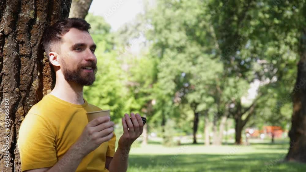 smiling man drinking from paper cup with closed eyes in park smiling man drinking from paper cup with closed eyes in park