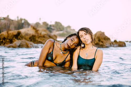 A romantic and beautiful couple of a black and a blonde woman in the water of the sea in a mediterranean beach in the sunset time of summer