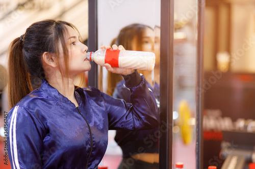 Young asian woman drinking protein shake from bottle after workout exercise for muscle at fitness gym healthy.