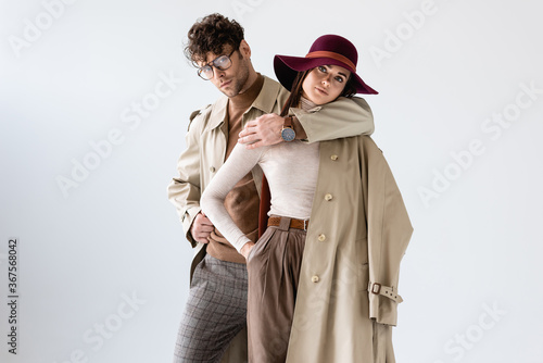 Obraz na płótnie stylish man hugging trendy woman while posing in autumn outfit isolated on grey