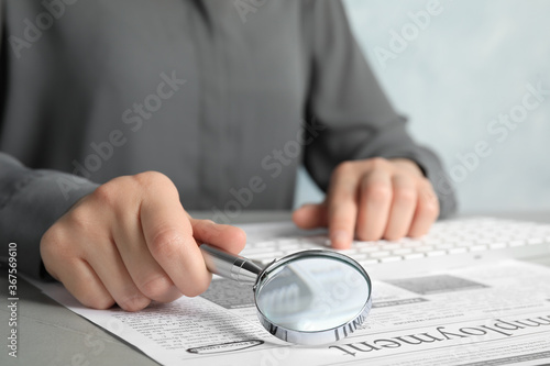 Woman looking through magnifying glass at newspaper, closeup. Job search concept