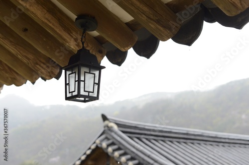 Closeup of a lamp hanging from a roof of a building surrounded by hills covered in the fog in Andong
