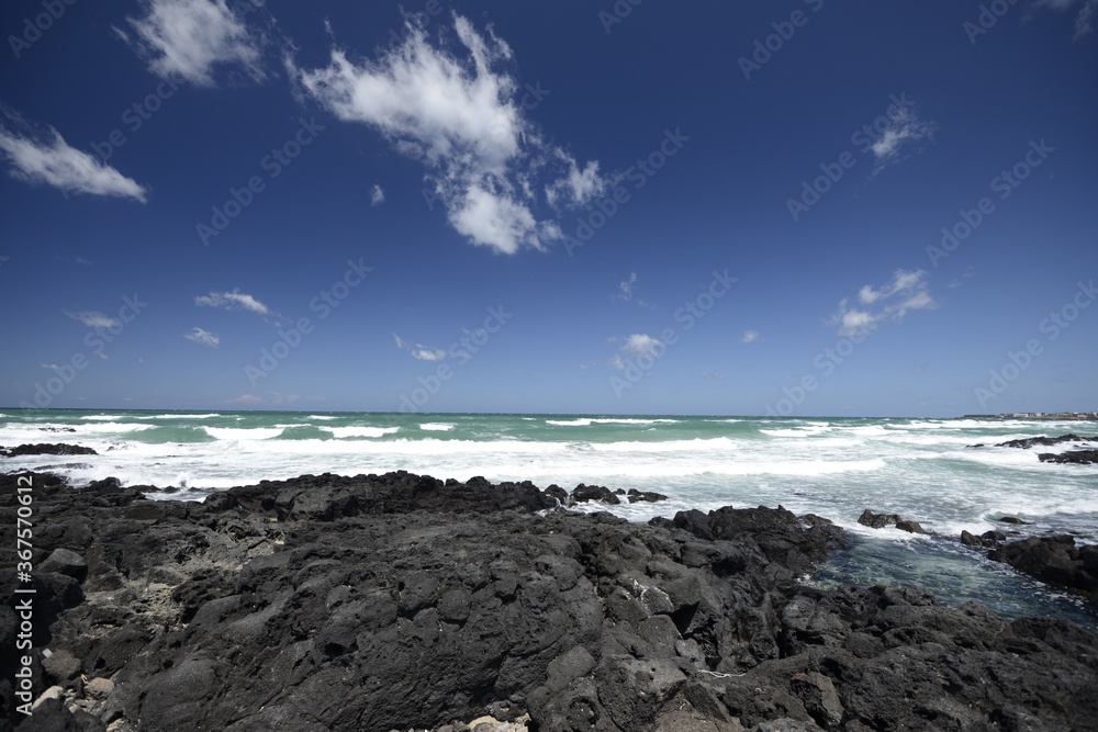 Beautiful shot of the coast on a cloudy blue sky background in Jeju Island, South Korea Beautiful shot of the coast on a cloudy blue sky background in Jeju Island, South Korea