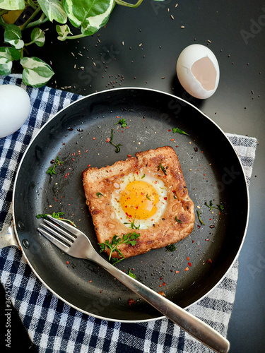 Egg in a hole topped with chili flakes, oregano, and herbs on a pan.