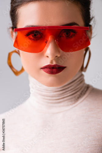 Portrait of beautiful woman in red sunglasses looking at camera isolated on grey
