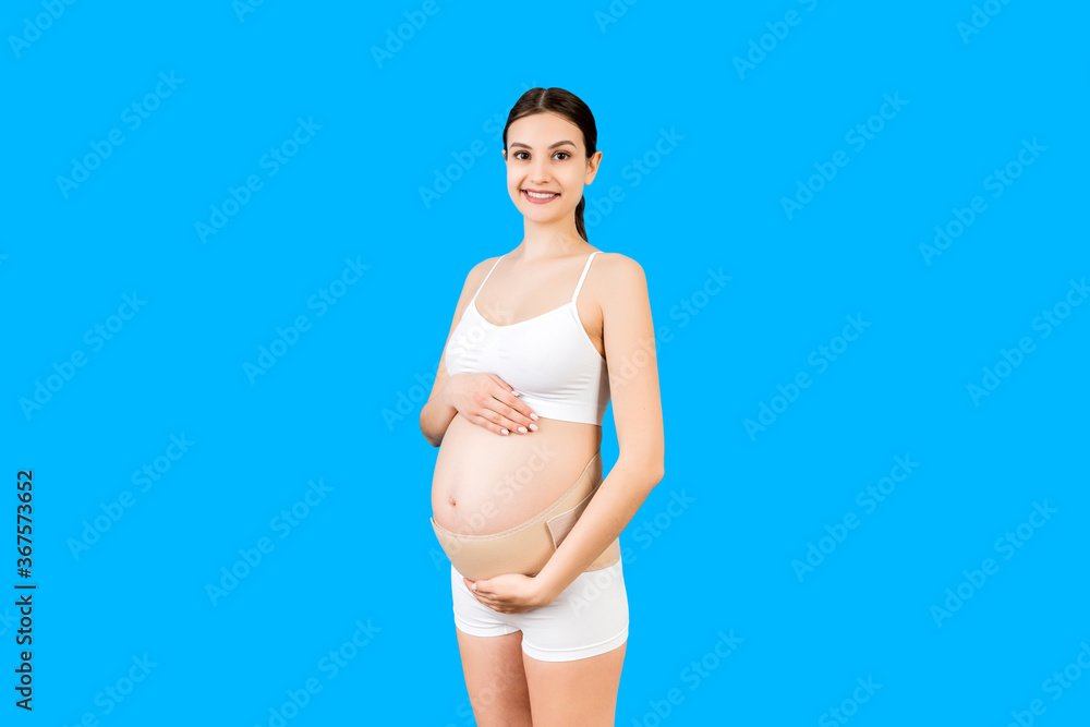 Portrait of pregnancy bandage dressed on pregnant woman in underwear for reducing backpain at blue background with copy space. Orthopedic abdominal support belt concept Portrait of pregnancy bandage dressed on pregnant woman in underwear for reducing backpain at blue background with copy space. Orthopedic abdominal support belt concept