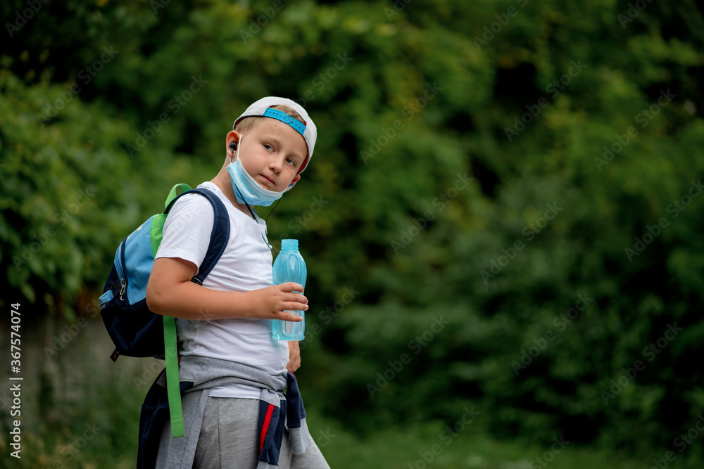 Back to school. Cool little schoolboy drinking water. Boy wearing a face mask down Back to school. Cool little schoolboy drinking water. Boy wearing a face mask down