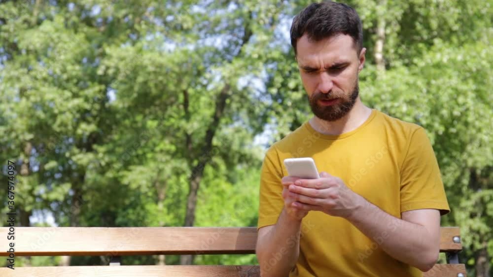 smiling man texting on smartphone on bench in park smiling man texting on smartphone on bench in park