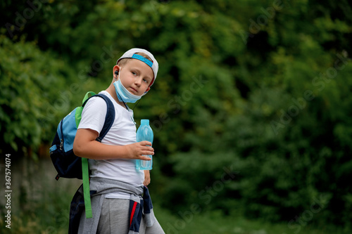 Back to school. Cool little schoolboy drinking water. Boy wearing a face mask down