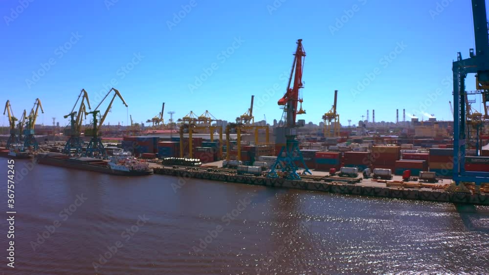 Aerial view of a row of construction or cargo cranes on the river bank. Ship docks off Kanonersky Island. Industrial port with water barges and transport tugs. Aerial view of a row of construction or cargo cranes on the river bank. Ship docks off Kanonersky Island. Industrial port with water barges and transport tugs.