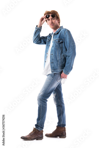 Flirtatious macho stylish young man holding sunglasses looking over shoulder. Full body length isolated on white background. 