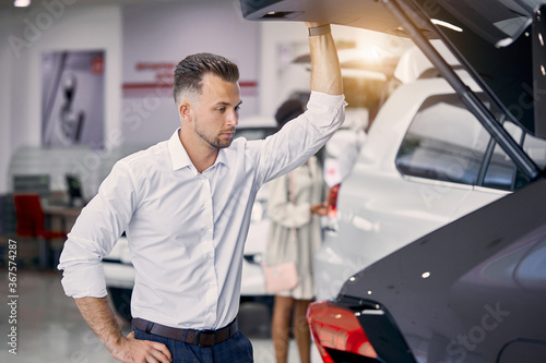 handsome caucasian businessman is examining a car before buying it  he checks all characteristics and features of auto