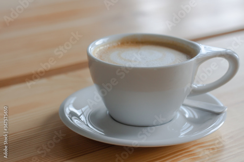 A white cup of coffee with foam on wooden background