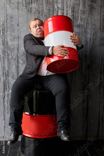 greedy caucasian fat oil tycoon hugs oil barrel. handsome businessman in formal wear engaged in oil production photo