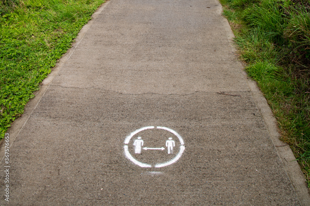 Obraz premium Social distancing painted sign on the floor at Caswell Bay Beach coastline path in Gower, Swansea Wales