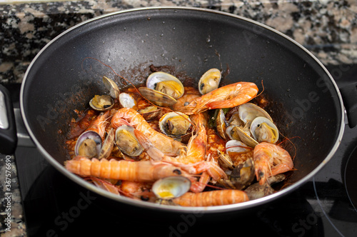 Spaghetti sauteed with clams and prawns in a pan in the kitchen of a house
