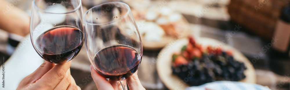 panoramic crop of couple clinking glasses with red wine