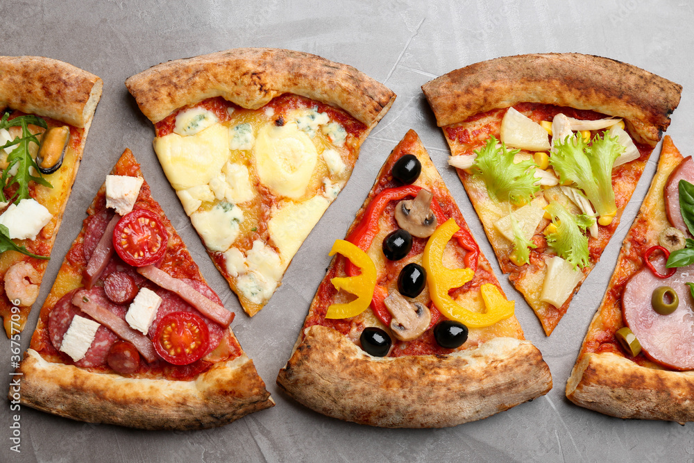 Slices of different delicious pizzas on grey table, flat lay Slices of different delicious pizzas on grey table, flat lay