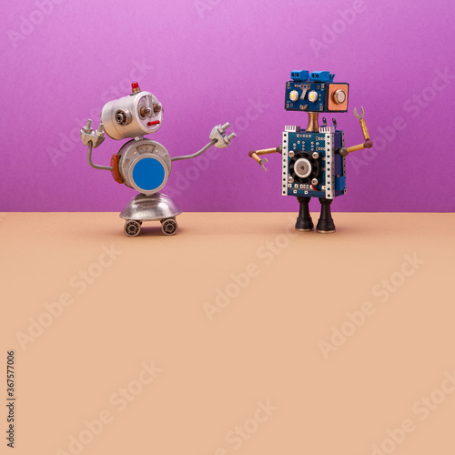 Meeting of two robots. A small robot on wheels welcomes a mechanical cyborg. Machine learning and artificial intelligence concept. Two electronic robotics toys on violet-beige background. copy space