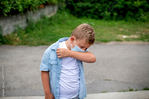 A young blond Caucasian boy demonstrating the correct way to cough and sneeze into an elbow rather than using hands to stop the spreading of the Corona virus during lock down 