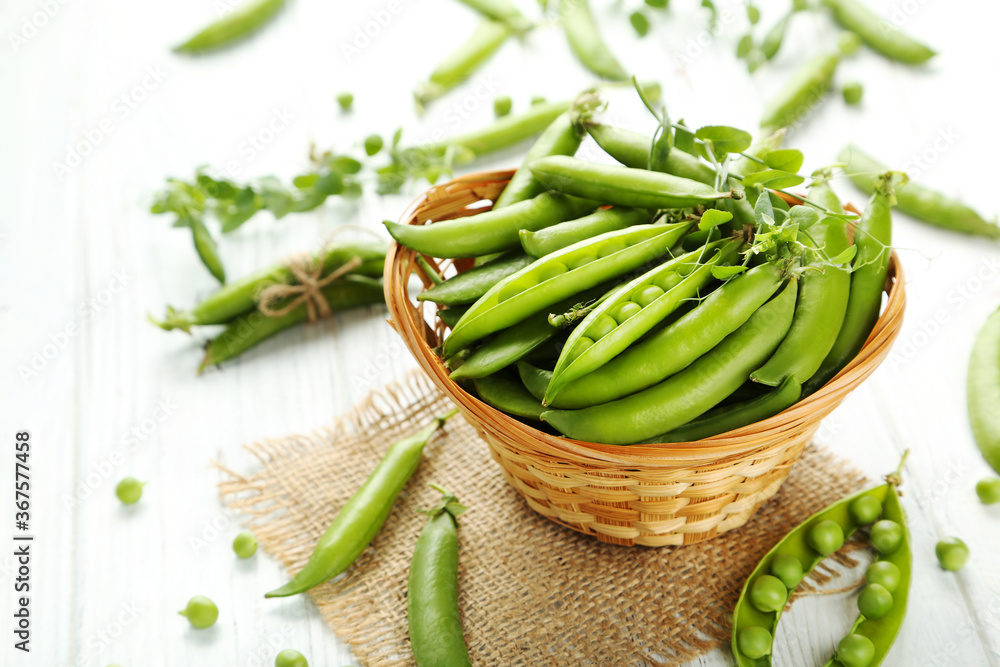 Green pea pods in basket on white wooden table Green pea pods in basket on white wooden table
