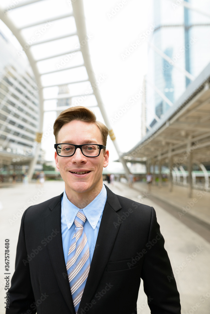 Happy young handsome blond businessman with eyeglasses in the city outdoors Happy young handsome blond businessman with eyeglasses in the city outdoors