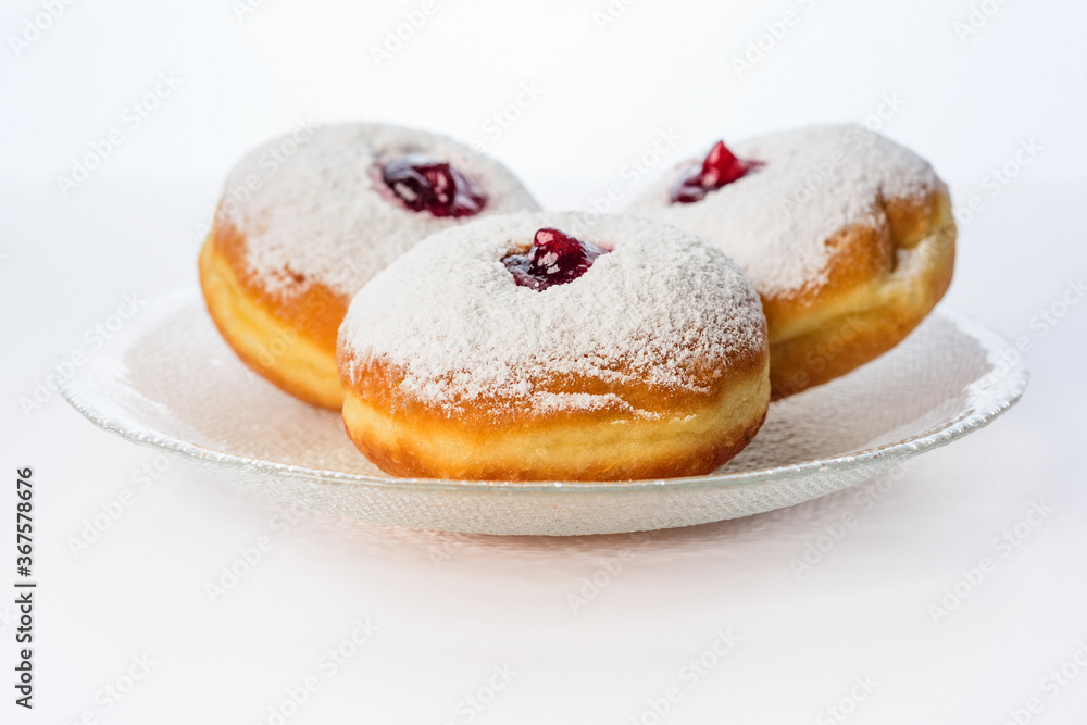 Three donuts on a glass plate on a white background decorated with sugar powder and strawberry jam