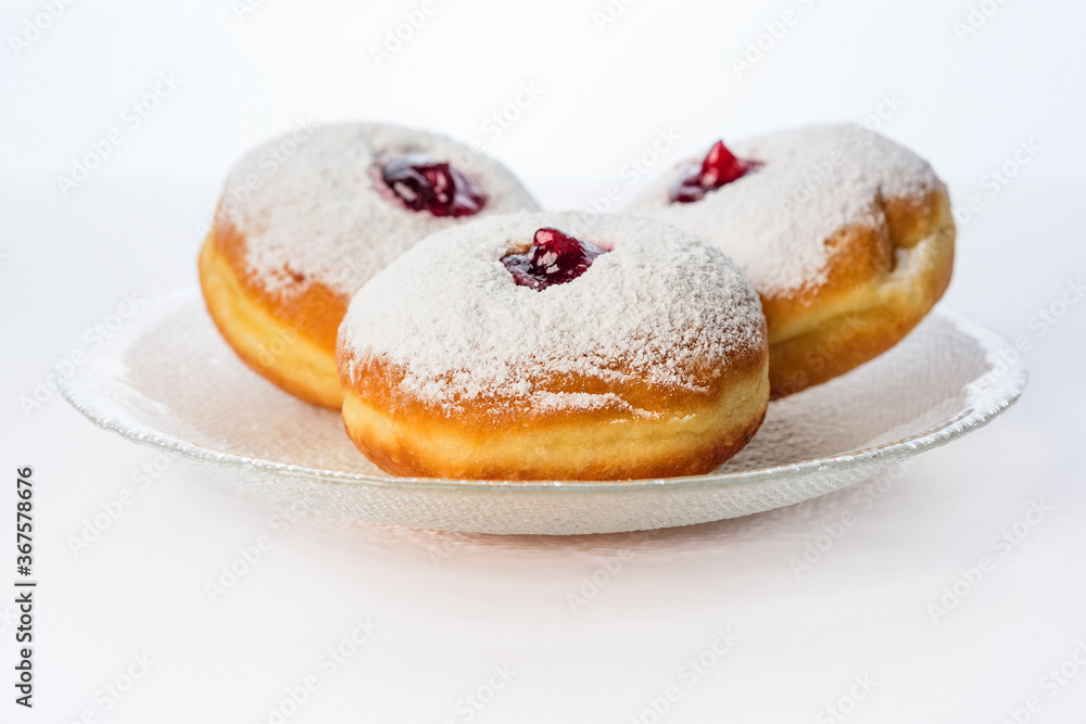 Three donuts on a glass plate on a white background decorated with sugar powder and strawberry jam Three donuts on a glass plate on a white background decorated with sugar powder and strawberry jam