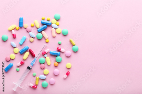 Colorful pills with syringe on pink background