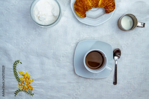 still life con taza de cafe con medialuna y jarra con leche sobre mantel blanco