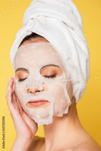 naked beautiful woman with closed eyes, towel on head and face mask isolated on yellow