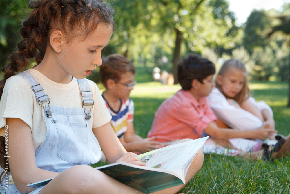 Cropped shot of a lovely young girl reading a book outdoors at the park on a warm summer day Cropped shot of a lovely young girl reading a book outdoors at the park on a warm summer day
