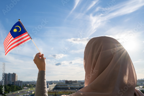 Silhouette of muslim woman in head scarf with Malaysia flag at blue sunset sky. Concept of freedom