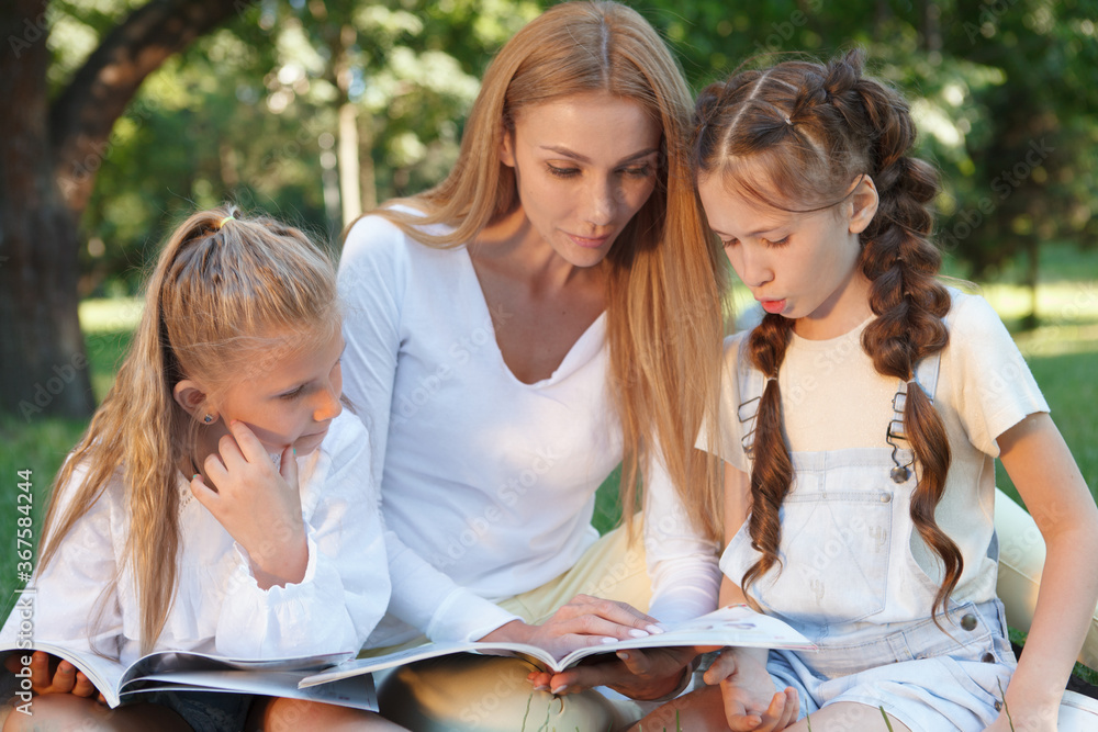 Lovely teacher and her female pupils reading together in the park Lovely teacher and her female pupils reading together in the park