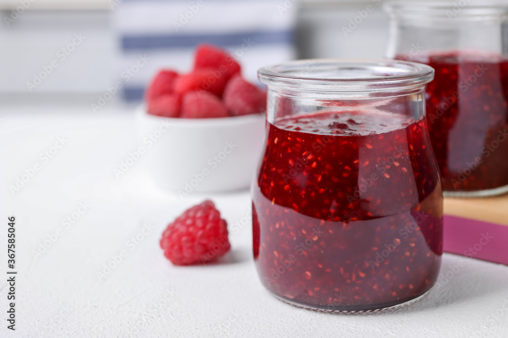 Delicious jam and fresh raspberries on white table, closeup. Space for text - obrazy, fototapety, plakaty 