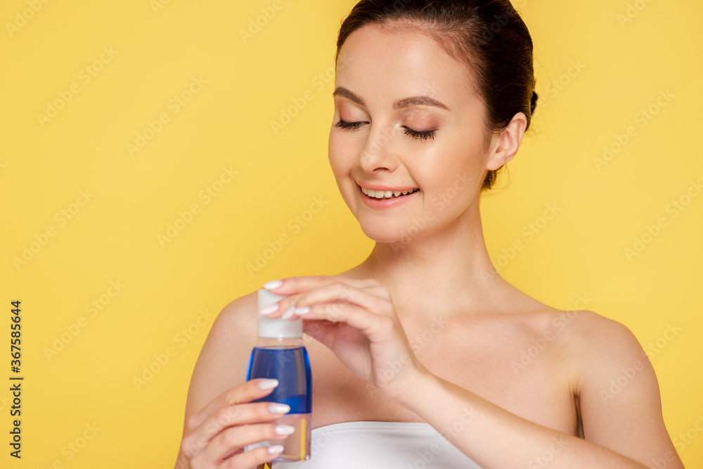 smiling beautiful woman holding micellar water in bottle isolated on yellow smiling beautiful woman holding micellar water in bottle isolated on yellow