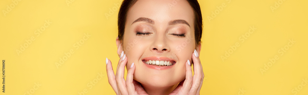 happy beautiful woman with closed eyes touching face isolated on yellow, panoramic shot