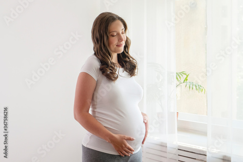 Free Download Portrait shot of young beautiful woman on third trimester of pregnancy. Close up of pregnant female with arms on her round belly. Expecting a child concept. Background, copy space. - GFXLoad