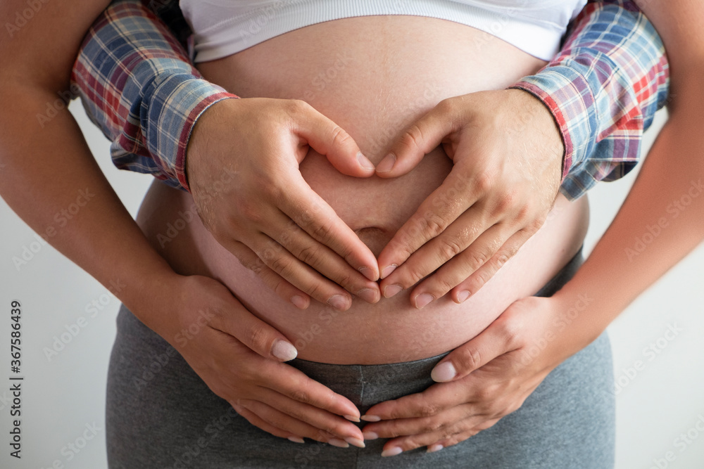 Close up shot of young man hugging his pregnant wife from behind, forming a heart shape with his hands over isolated white background. Prenatal period concept. Young family expecting a new child. Close up shot of young man hugging his pregnant wife from behind, forming a heart shape with his hands over isolated white background. Prenatal period concept. Young family expecting a new child.